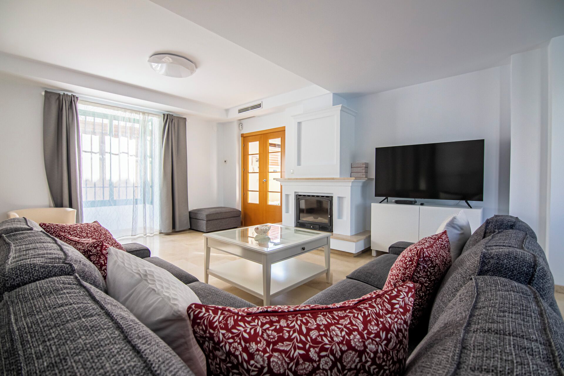 A modern living room with a sofa set, a glass coffee table, a fireplace, and a television mounted on the wall.