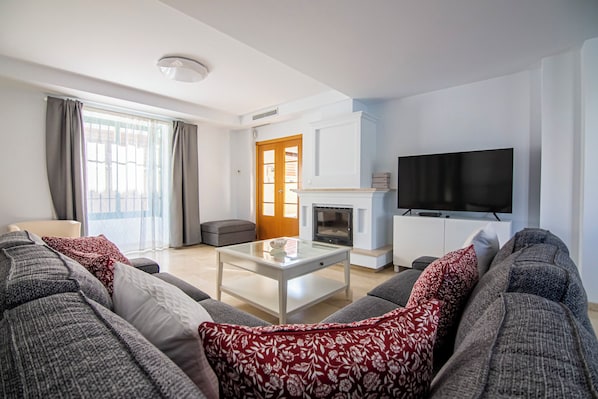 A modern living room with a sofa set, a glass coffee table, a fireplace, and a television mounted on the wall.