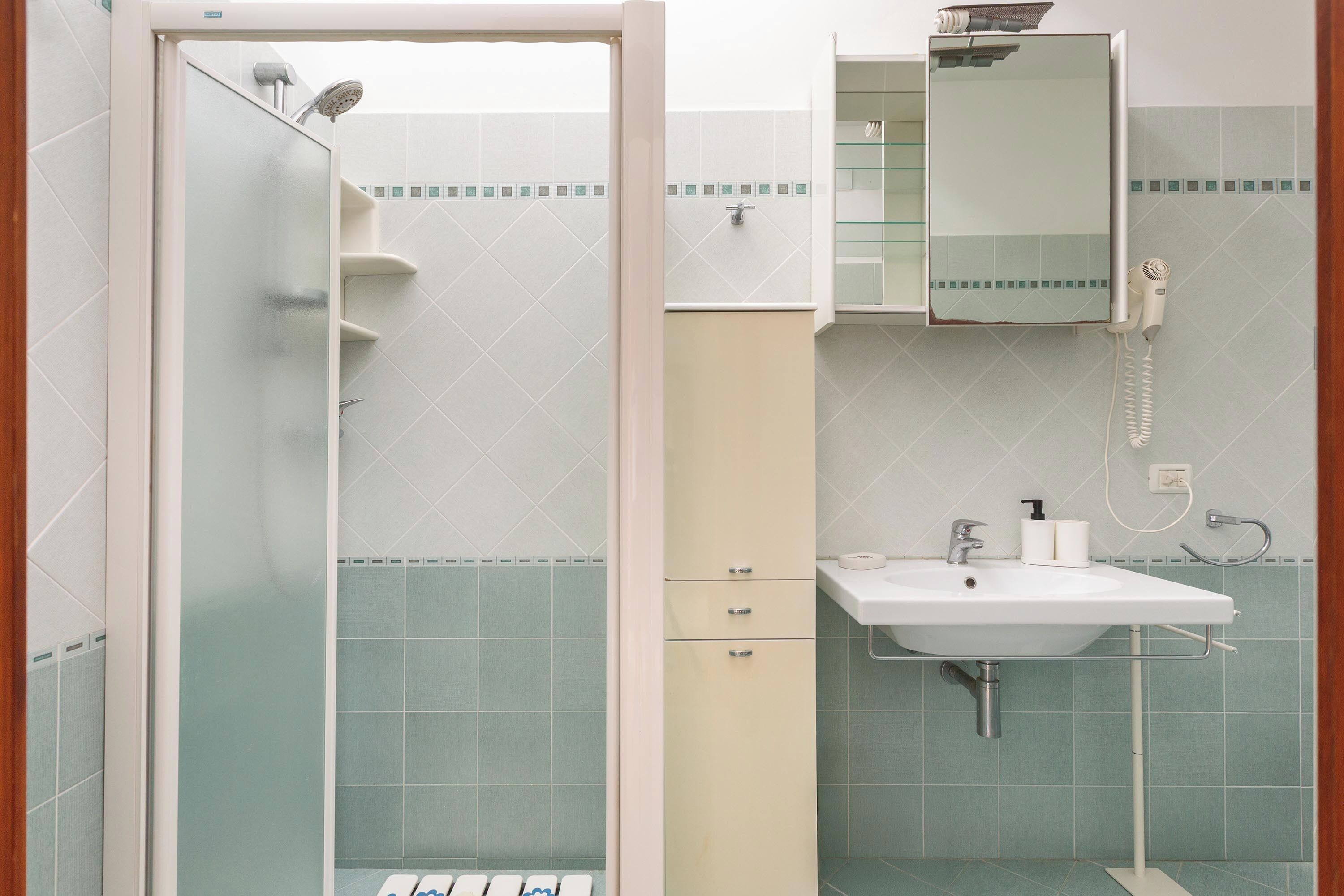 A bathroom with a shower, a sink, a mirror, and a cabinet.