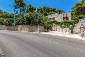 A road with a stone wall and a building with a stone facade and wooden shutters. - Villa Natura by BarbarHouse (Santa Cesarea Terme)