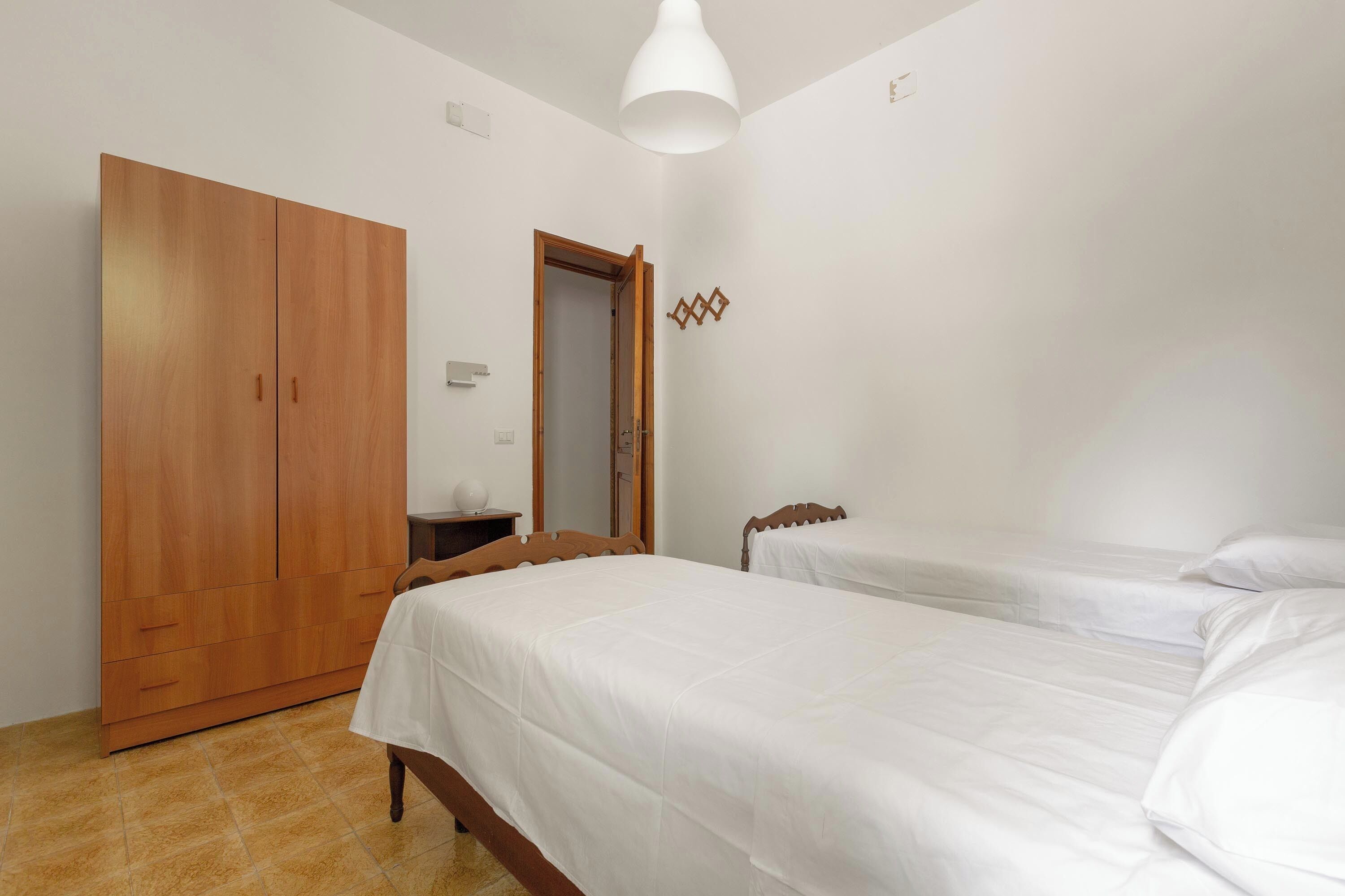 A bedroom with two beds, a wardrobe, and a door leading to another room.