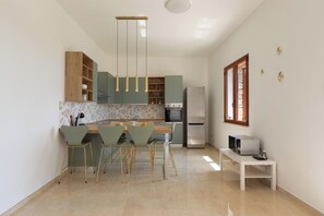 A modern kitchen with a dining area, featuring a central island, pendant lighting, and a refrigerator.