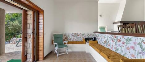 Una habitación con un banco, una silla, una pequeña mesa y vistas al exterior.