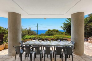 Ein Essbereich im Freien mit einem Tisch für sechs Personen, umgeben von Stühlen und Blick aufs Meer.
