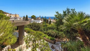 A garden with a stone bench, various plants, and a view of the sea and buildings in the distance. - Villa Natura by BarbarHouse (Santa Cesarea Terme)