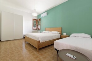 A hotel room with a bed, bedside table, and a wall-mounted air conditioning unit.