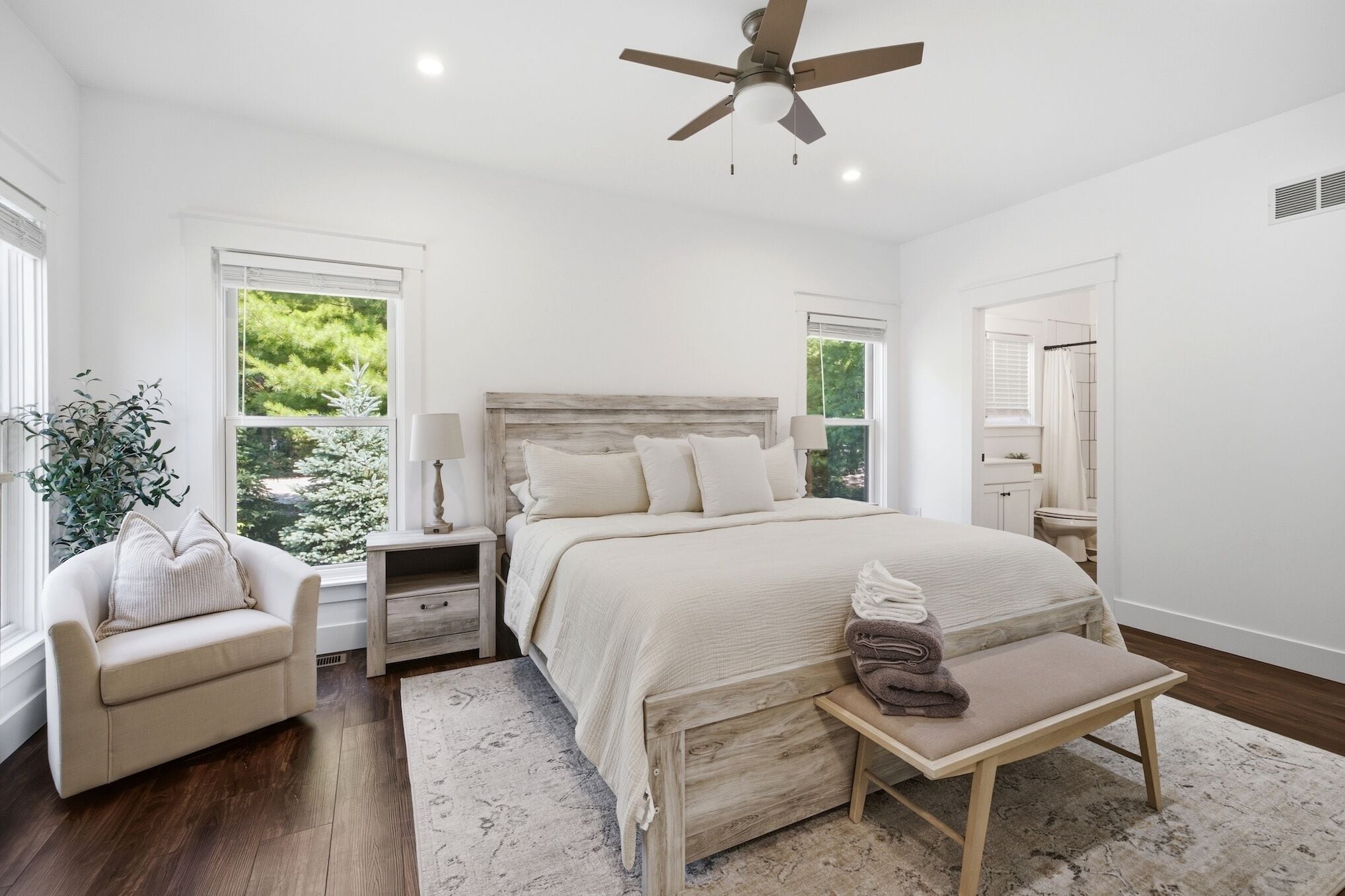 A bedroom with a bed, bedside tables, a chair, a bench, and a ceiling fan.