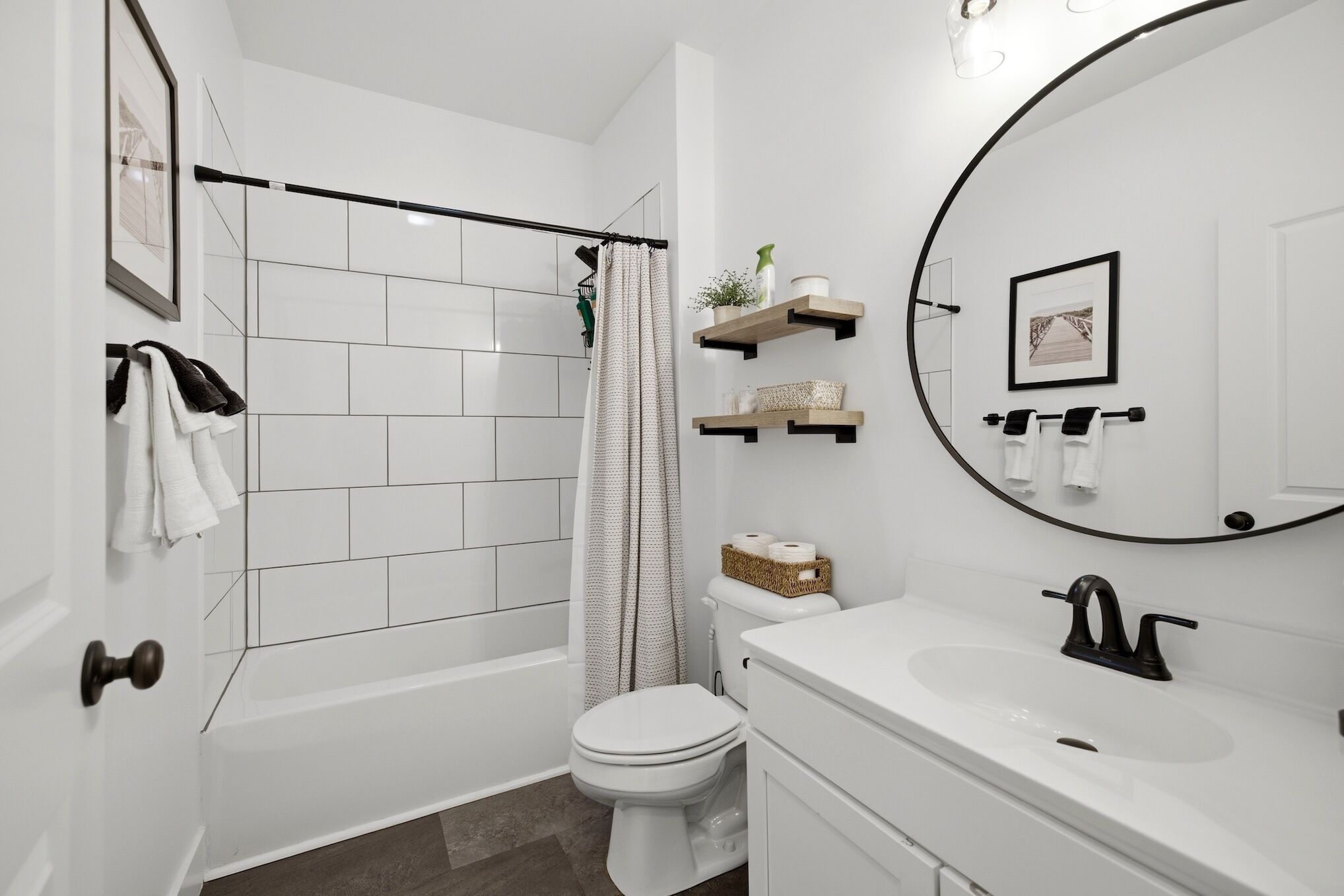 A modern bathroom with a bathtub, toilet, and sink. There are towels hanging on a rack, a shower curtain, and a mirror above the sink.