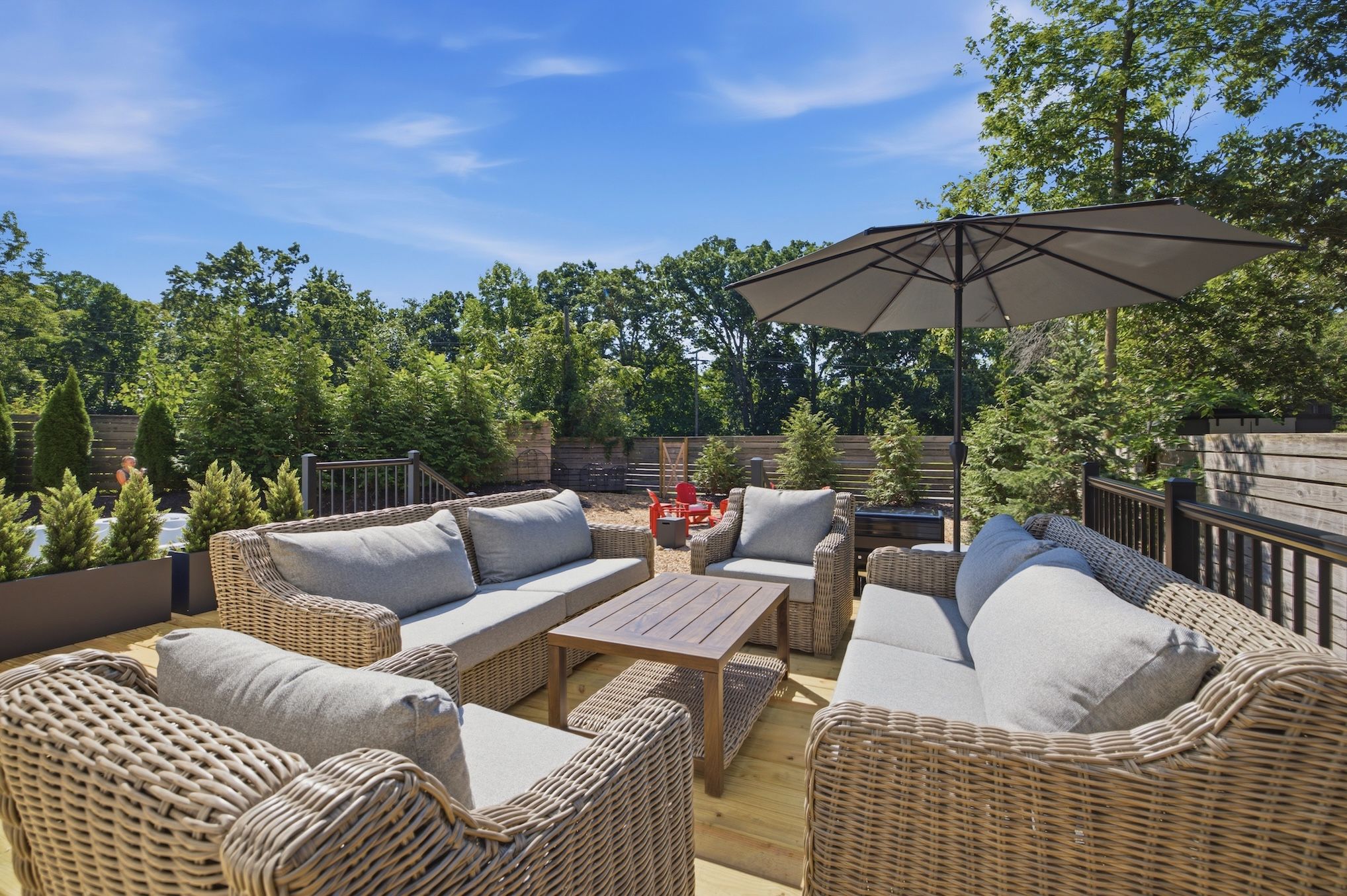 An outdoor patio with wicker furniture, a wooden table, and a large umbrella.