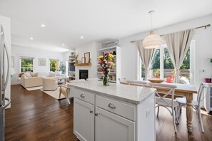 A modern kitchen with a central island, white cabinetry, and a dining area with a wooden table and chairs. - It's A Wonderful Life - Union Pier, MI (New Buffalo)