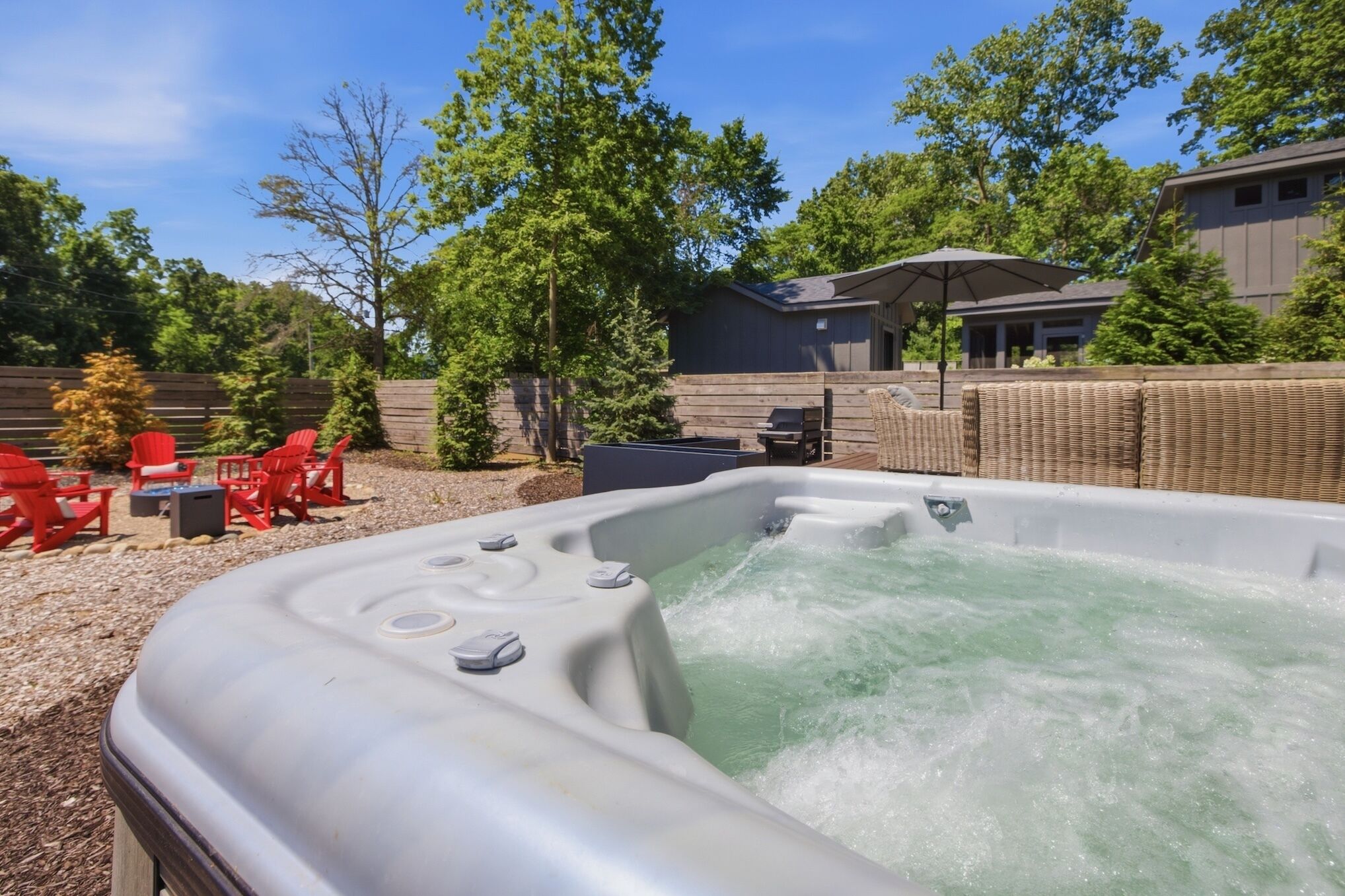 Ein Whirlpool mit einer Holzterrasse und roten Stühlen, umgeben von Bäumen und einem Holzzaun.