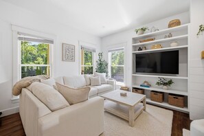 A modern living room with a sofa, coffee table, and TV. There are windows with views of greenery. - It's A Wonderful Life - Union Pier, MI (New Buffalo)