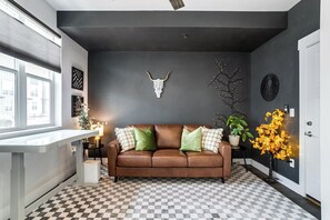 A modern living room with a checkered floor, a brown leather sofa, decorative wall art, and a potted plant. - Stylish Denver Retreat Townhome (Denver)