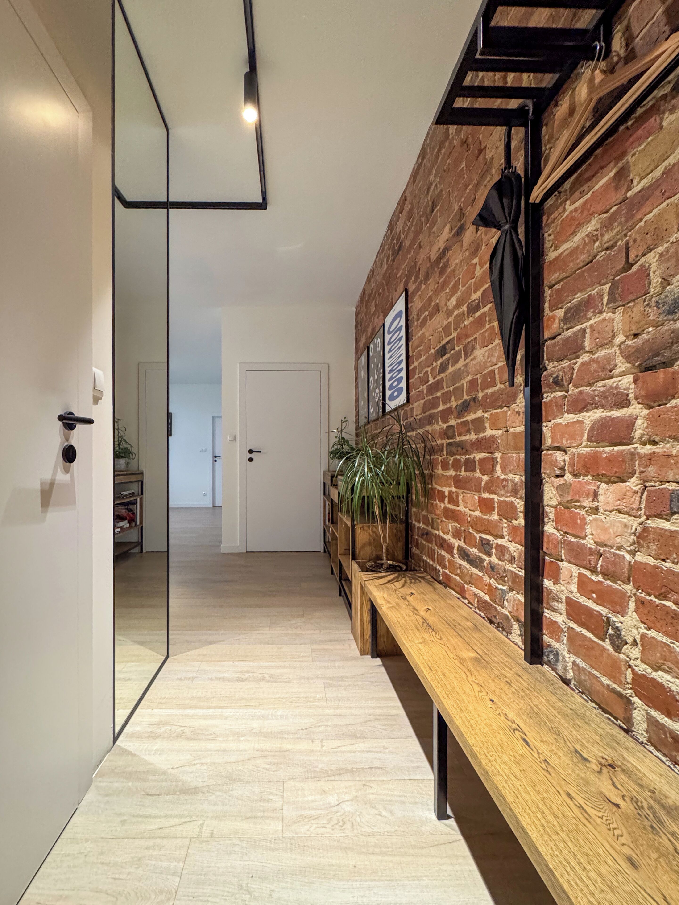 A hallway with a wooden bench, a brick wall, and a door leading to another room.