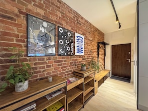 A brick wall with two framed artworks, a wooden console table with books and a plant, and a door in the background. - Fully equipped serviced apartment for modern & independent explorers. (Katowice)