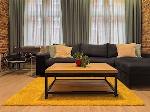 A modern living room with a black sectional sofa, a wooden coffee table, and a yellow rug. - Fully equipped serviced apartment for modern & independent explorers. (Katowice)