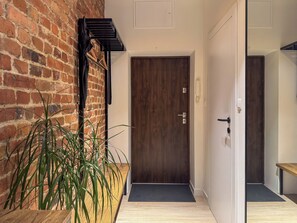 A hallway with a wooden door, a brick wall, and a potted plant. - Fully equipped serviced apartment for modern & independent explorers. (Katowice)