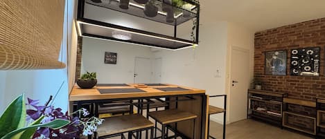 Una cocina moderna con una mesa de madera, sillas negras y un estante con plantas colgantes.