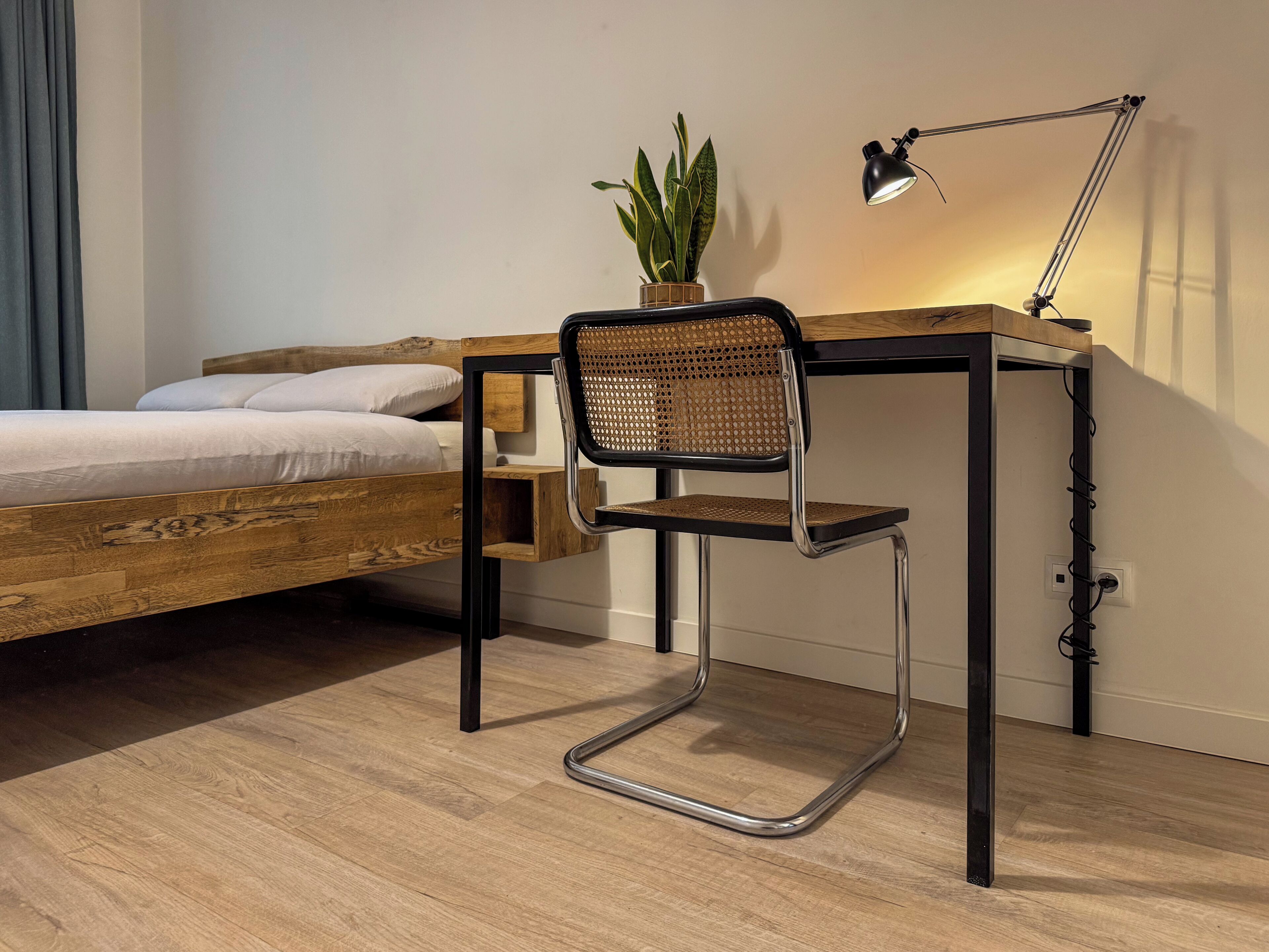 Une chambre à coucher avec un lit en bois, un bureau avec une chaise, une plante en pot et une lampe de bureau.