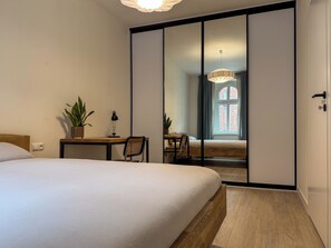 A bedroom with a bed, bedside table, lamp, potted plant, and a sliding door leading to a bathroom. - Fully equipped serviced apartment for modern & independent explorers. (Katowice)