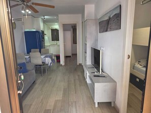 Ein modernes Wohnzimmer mit Flachbildfernseher auf einem Schrank, einem Essbereich mit Tisch und Stühlen sowie einer Küchenzeile mit Schränken und Spüle.