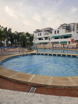 Ein Pool mit Liegestühlen und Palmen, umgeben von Gebäuden mit Balkonen.