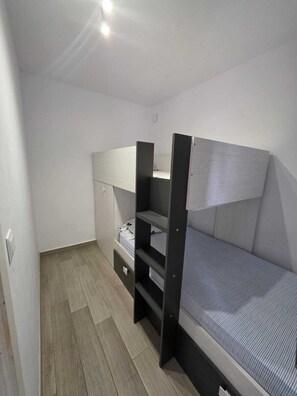 Ein kleines Zimmer mit einem Stockbett, einem kleinen Schreibtisch und einem Kleiderschrank.