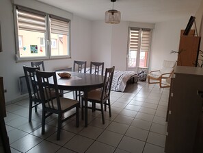 Una habitación con una mesa de comedor, sillas, una cama, un ventanal y una lámpara colgante.