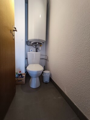 Un baño pequeño con inodoro, un cubo de basura y calentador de agua.