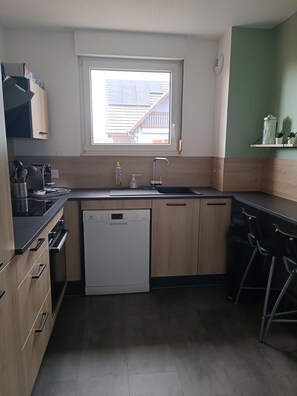 A compact kitchen with a dishwasher, a sink, and a window overlooking a residential area. - Vrbo Property (Geispolsheim)