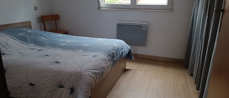 Ein Schlafzimmer mit einem Bett, einem Heizkörper, einem Fenster mit Jalousien und einem Vorhang.