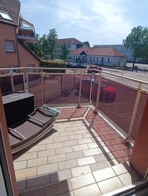A covered outdoor area with a seating area, a fence, and a view of the street and buildings in the background. - Cozy apartment with a balcony for 4 people near Strasbourg, Colmar, and Europapark (Geispolsheim)