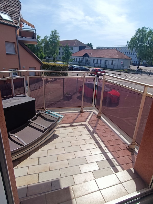 Un espacio al aire libre cubierto con zona de estar, una valla y vistas a la calle y edificios al fondo.