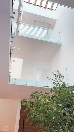A multi-level interior with glass railings and a plant. - Casa Nueva con Alberca y Rooftop con Vista al Mar! (Isla Mujeres)