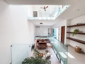 A modern interior with a glass railing, a dining area, and a ceiling fan. - Casa Nueva con Alberca y Rooftop con Vista al Mar! (Isla Mujeres)