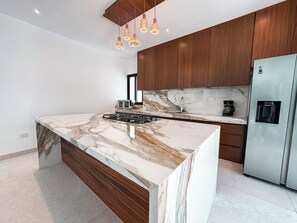 A modern kitchen with a marble island, stainless steel appliances, and wooden cabinets. - Casa Nueva con Alberca y Rooftop con Vista al Mar! (Isla Mujeres)