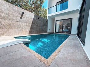 A modern outdoor swimming pool with a stone wall and a glass door leading to a balcony. - Casa Nueva con Alberca y Rooftop con Vista al Mar! (Isla Mujeres)