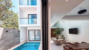 En moderne bygning med swimmingpool, udendørs siddepladser og et vægmonteret fladskærms-tv.