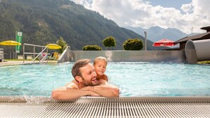 Ein Schwimmbecken mit Blick auf das Gebirge, einer Rettungsschwimmerstation und einem roten Sonnenschirm.