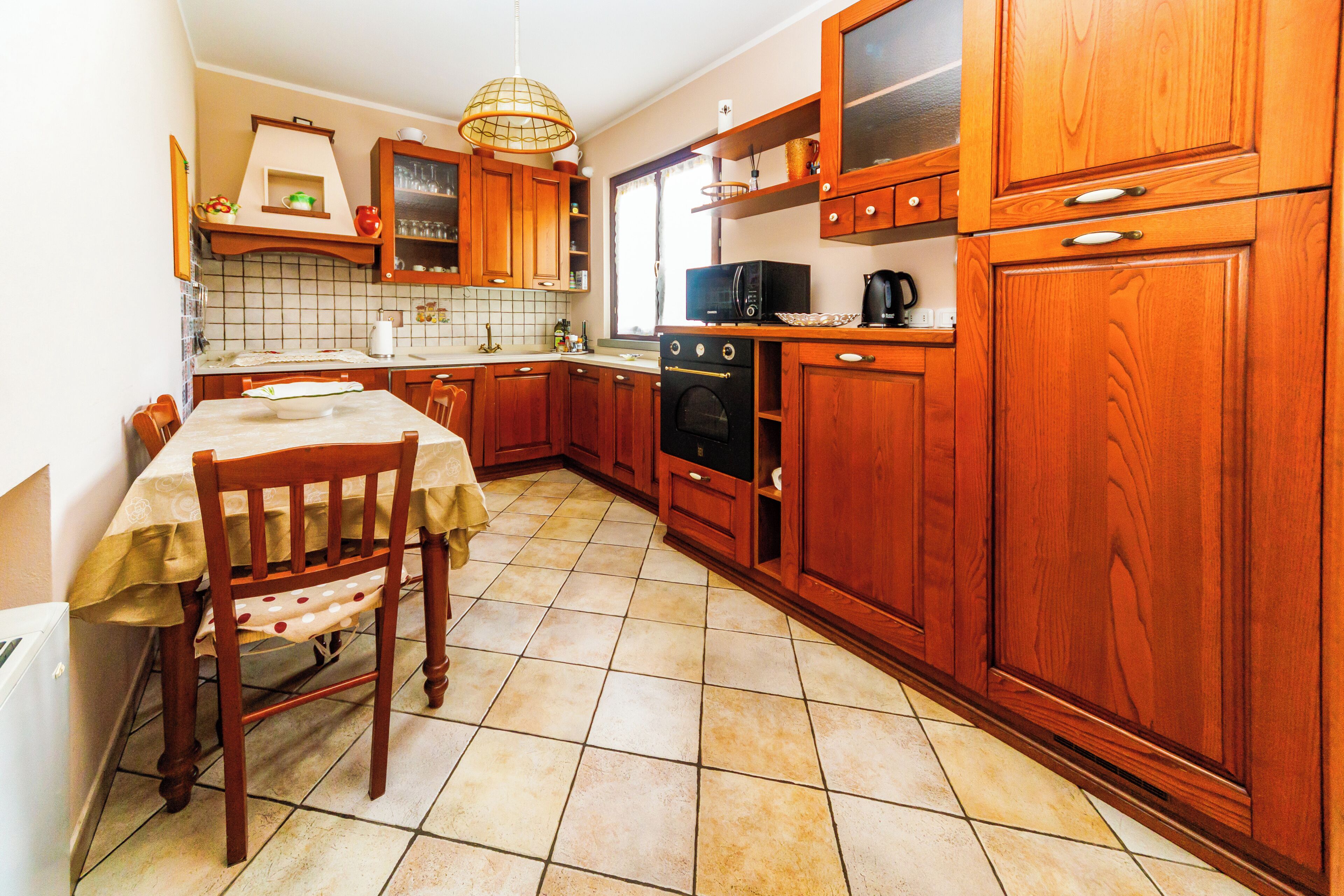 Une cuisine avec des meubles de rangement en bois, une table à manger avec des chaises et un sol carrelé.
