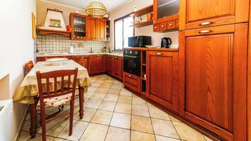 Une cuisine avec des meubles de rangement en bois, une table à manger avec des chaises et un sol carrelé.