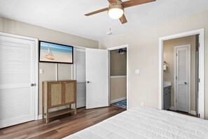 A bedroom with a bed, a ceiling fan, a wooden cabinet, a closet with a sliding door, and a wall-mounted TV. - Walkable to Beach, Family Friendly (Miramar Beach)