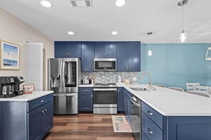 A modern kitchen with blue cabinets, stainless steel appliances, a white countertop, and a blue accent wall. - Walkable to Beach, Family Friendly (Miramar Beach)