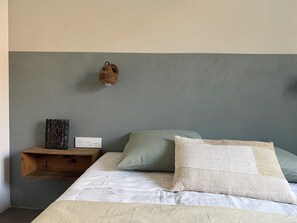 Ein Schlafzimmer mit einem Bett, Kissen, einem Nachttisch, einer Wandlampe und einer Steckdose.