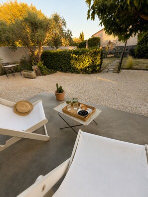 Un patio con due poltrone bianche, un tavolino con un vassoio di bevande e olive, e un cactus in vaso.