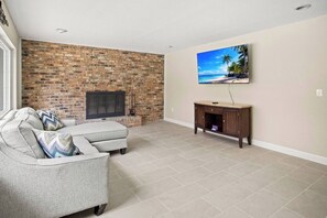 A living room with a brick fireplace, a grey sofa, and a TV mounted on the wall. - Gem at Crystal River (Crystal River)