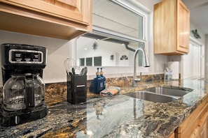 A kitchen with a coffee maker, a spice rack, and a sink. - Gem at Crystal River (Crystal River)