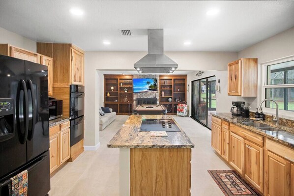 A modern kitchen with a central island, wooden cabinets, and a built-in stove. - Gem at Crystal River (Crystal River)