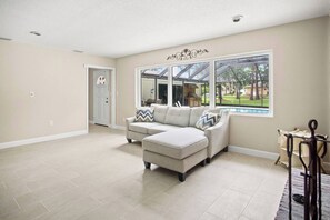 A spacious living room with a sectional sofa, a dining area with a table and chairs, and a large window offering a view of the outdoors. - Gem at Crystal River (Crystal River)