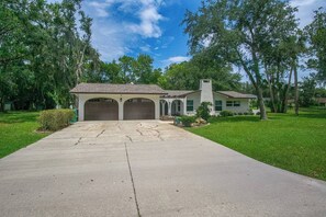 A residential house with a driveway leading to a garage, surrounded by trees and grass. - Gem at Crystal River (Crystal River)